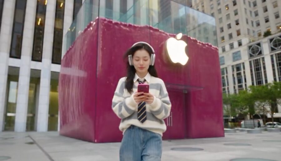 Eine junge Frau mit Kopfhörern und Smartphone läuft vor einem pinkfarbenen Apple Store.